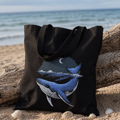Black tote bag with whale design on a beach