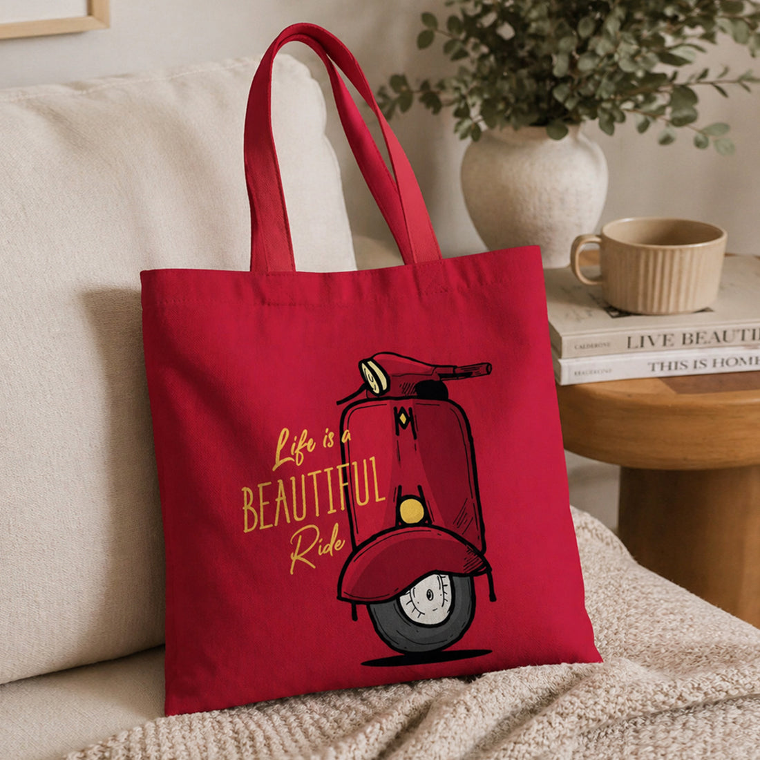 Red tote bag with scooter graphic and 'Life is a Beautiful Ride' text on a couch.