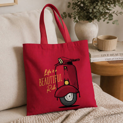 Red tote bag with scooter graphic and 'Life is a Beautiful Ride' text on a couch.