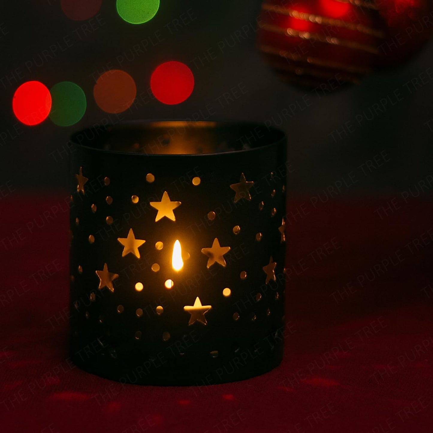 Black candle holder with star designs holding a lit candle against a dark background with colorful lights.