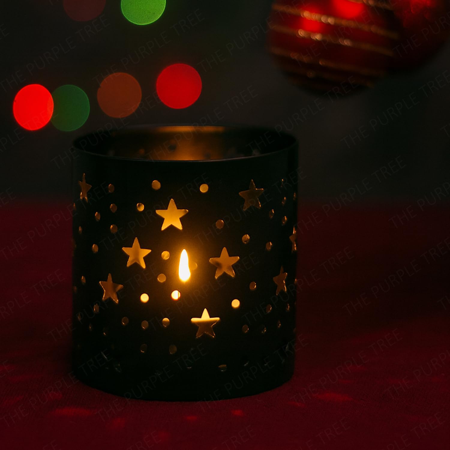 Black candle holder with star designs holding a lit candle against a dark background with colorful lights.