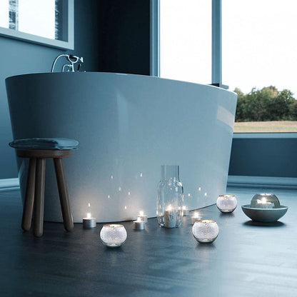 A bathtub with illuminated candles and a stool in front of it.