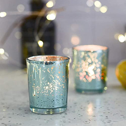  Lit candles in a teal glass holder next to a small plate.