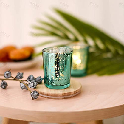 A teal glass candle holder with lit candles and a small plate on a table.