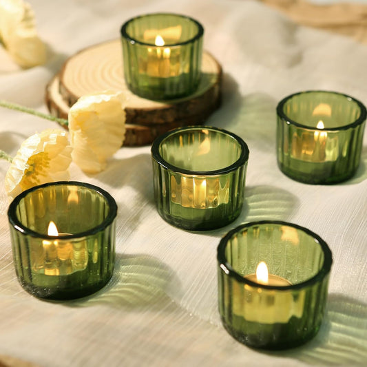 Green glass candle holders with lit candles on a white fabric background