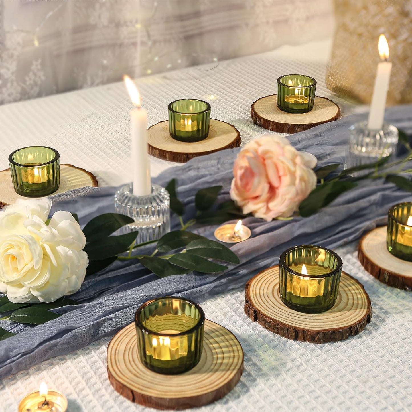 Decorative setup with green candle holders on wooden coasters, candles, and flowers on a textured surface.