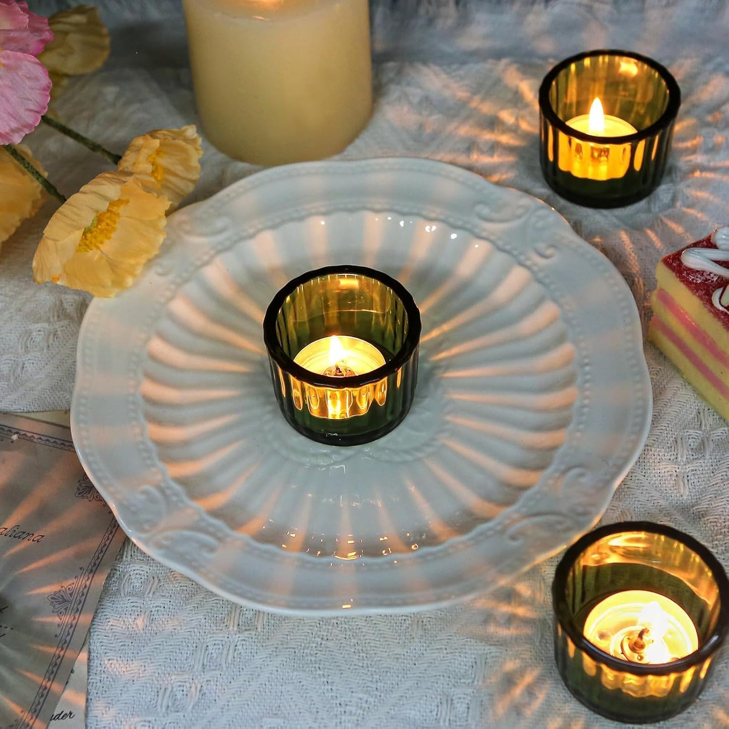 Candle holders with lit candles on a textured surface with flowers and a cake.