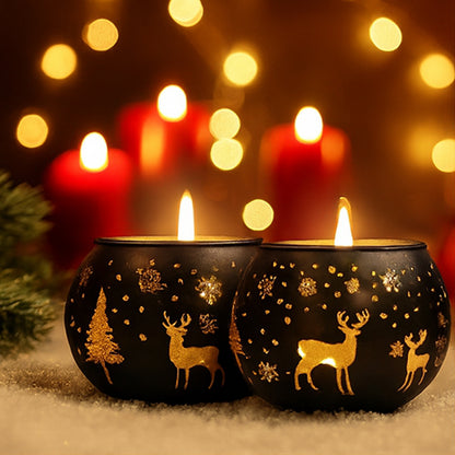 Two lit candles in black holders with gold deer and tree designs, against a warm, blurred lights background.