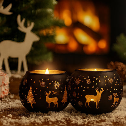 Two lit candle holders with deer and tree designs in front of a fireplace and Christmas decorations.