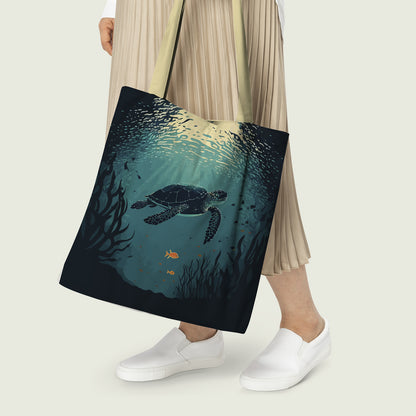 A person holding a tote bag with an underwater design featuring a turtle swimming among seaweed and small fish, with light rays filtering through the water from above.