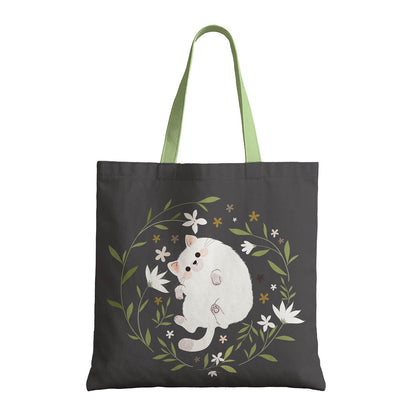 A tote bag displaying a white cat with a backdrop of assorted flowers.