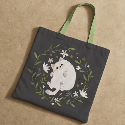 A tote bag showcasing a playful white cat among blooming flowers.