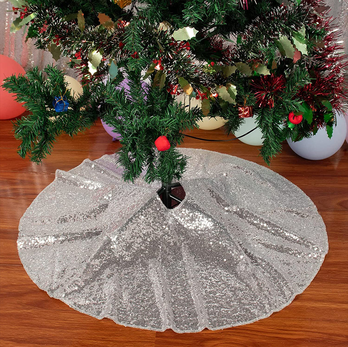Silver sequin tree skirt under a decorated Christmas tree on a wooden floor.