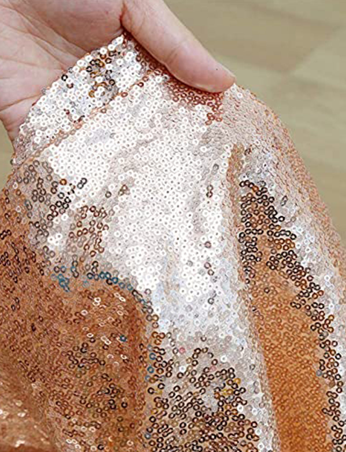 Close-up of a hand holding a piece of fabric with rose gold sequins.