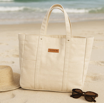Beige tote bag with sunglasses and a hat on a sandy beach