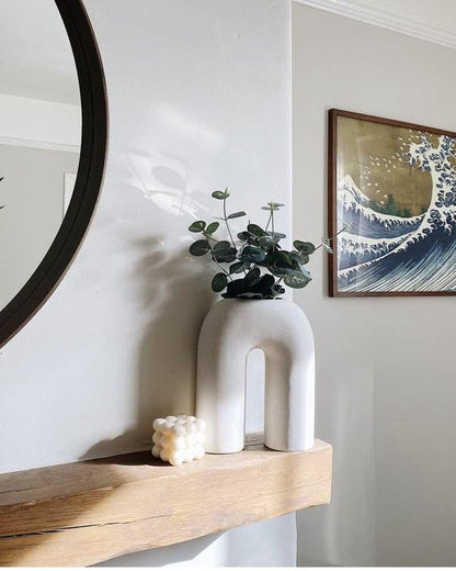 A white vase with a plant on a shelf.