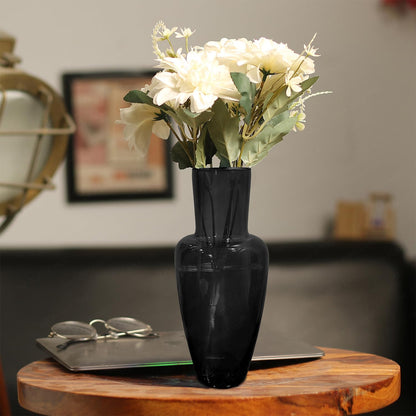 A black vase filled with white flowers elegantly placed on a wooden table.
