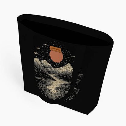 A black tote bag displaying a picturesque mountain scene with a sun, ideal for outdoor enthusiasts.