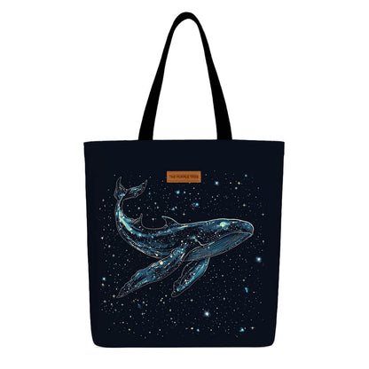 A tote bag featuring a whale design surrounded by stars on a light background.
