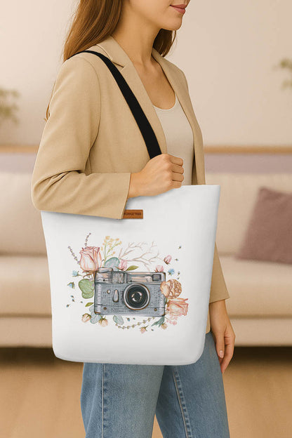  A white tote bag displaying an image of a camera with vibrant flowers in the background.
