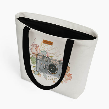 A white tote bag adorned with a photograph of a camera and blooming flowers.